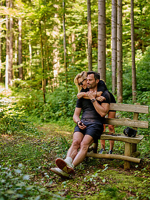 Paar umarmt sich auf rustikaler Holzbank im üppigen Wald