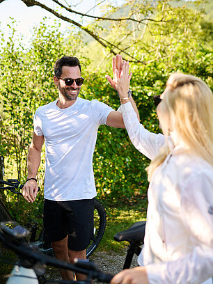 Mann und Frau geben sich in einem sonnigen Park ein High-Five neben Fahrrädern