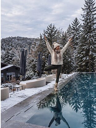 Person in Yoga-Pose neben Pool im verschneiten Bergresort, in Winterkleidung