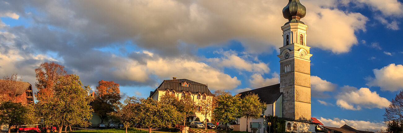 Kirchturm und Gebäude mit grünem Rasen unter teils bewölktem Himmel